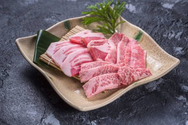 Siyah arka planda beyaz tabakta çiğ et parçaları var.