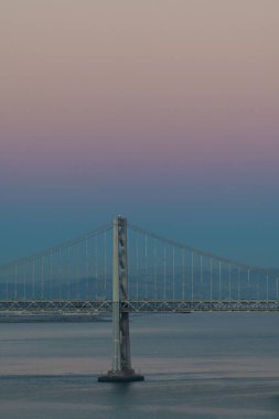 Oakland Bay Köprüsü 'nün San Francisco, Kaliforniya' da pembe ve mavi bir gökyüzünün altında dikey görüntüsü.