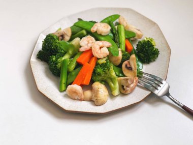 Beyaz tabakta servis edilen karidesli kızarmış sebzelerin yüksek açılı görüntüsü.