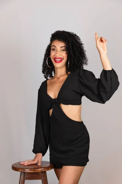 stock image Portrait of a young woman standing next to a wooden stool, pointing up. Against white background in studio