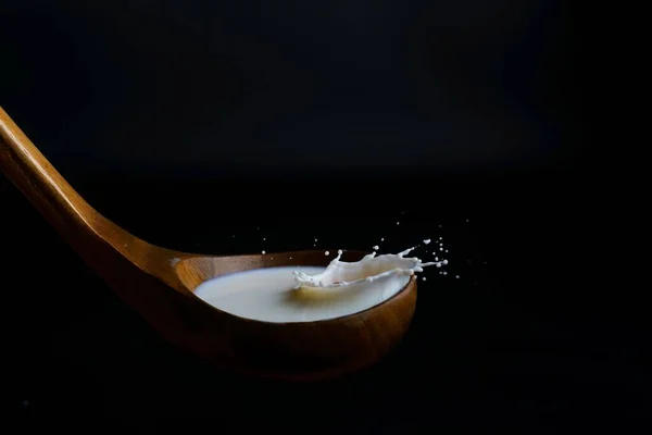 牛奶溅在木制勺子上 具有溅溅效果和黑色背景 — 图库照片