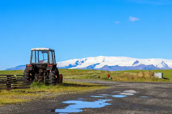 Ciągnik Zaparkowany Trawie Przed Pokrytą Śniegiem Górą — Zdjęcie stockowe