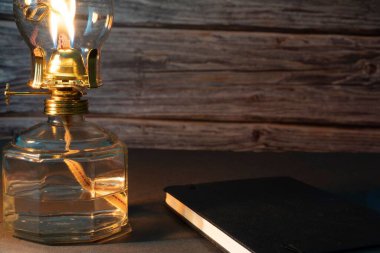 Yakından çekilmiş bir gaz lambası ve arka planda ahşap bir duvar olan kapalı bir kitap.
