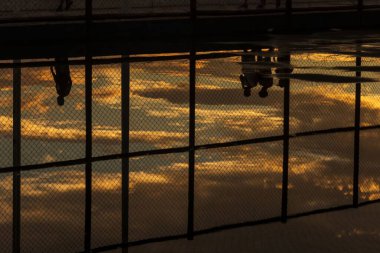 Salvador, Bahia 'daki Rio Vermelho plajında, sarı günbatımına karşı egzersiz yapan insanların siluetinin yansıması..