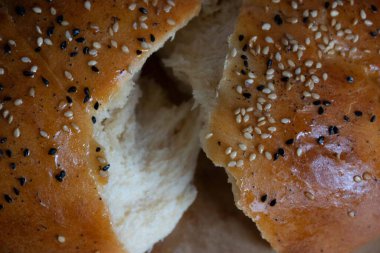 Parlak bir kabukla örülmüş, nigella ve susam tohumları serpiştirilmiş altın bir çöreğin yakın plan çekimi.
