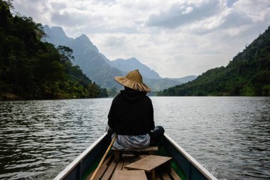 Nong Khiaw, Laos Dağları 'ndaki Nam Ou Nehri' ndeki teknede hasır şapkalı Asyalı çocuk.