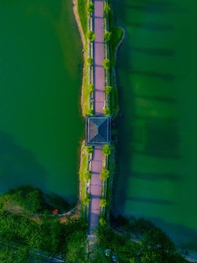 Yeşil nehir suyu üzerinde yeşil ağaçların yakınındaki bir köprünün insansız hava aracı görüntüsü.