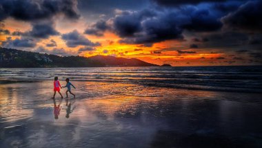 Phuket Patong plajında gün batımı bulutlu gökyüzü ile oynayan çocukların manzarası.