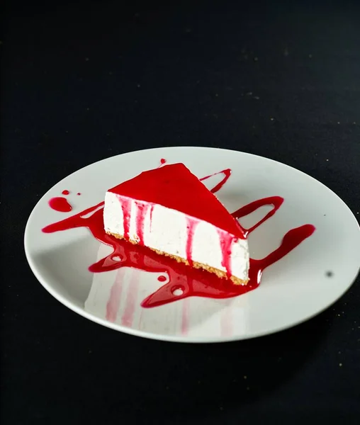 A vertical shot of a strawberry cheesecake on a black surface