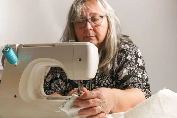 Beyaz Saçlı Yaşlı Kadın Dikiş Makinesine Beyaz Bir Kumaş Dikiyor — Stok fotoğraf