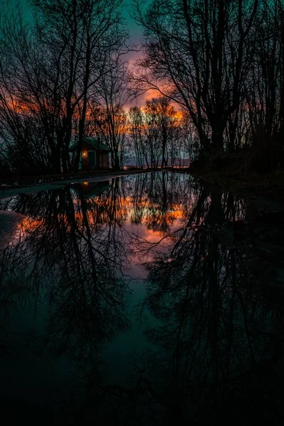 森の中の湖の海岸に小さなキャビンで 水面に沈む夕日の魅惑的な反射 — ストック写真