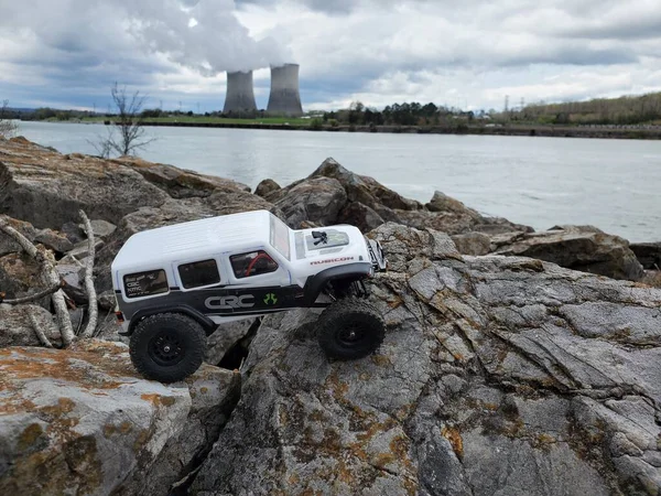 在湖边的石头上挂着一辆玩具车吉普 兰格勒 它的目标是核电站 — 图库照片