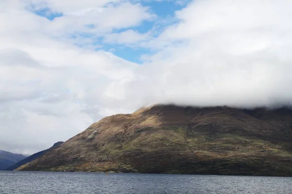 青い空の白い雲が湖によって丘に触れる景色 — ストック写真