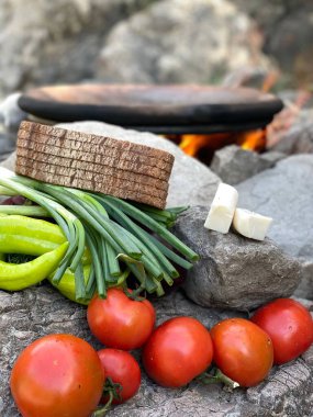 Gündüz vakti bir evin bahçesindeki kayalıklarda ekmek, peynir ve sebzelerden oluşan dikey bir kare.