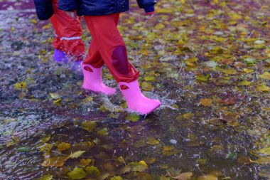 Yağmurlu bir günde iki çocuk botlarıyla su birikintisinde yürüyor.