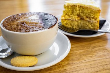 Bir fincan cappuccino ve masanın üzerinde bir parça kek.