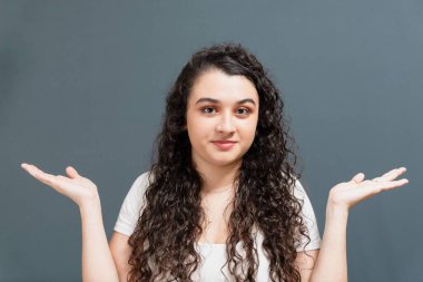 Neşeli genç ve güzel bir kadın kollarında jestlerle neler olduğunu soruyor. Gri arkaplanda izole.