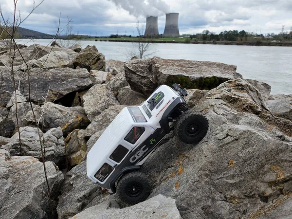 在湖边的石头上挂着一辆玩具车吉普 兰格勒 它的目标是核电站 — 图库照片