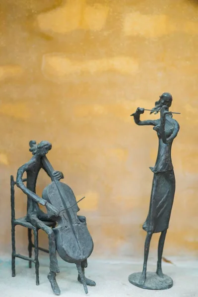 在黄色背景上演奏小提琴和小提琴的两个雕塑的竖直照片 — 图库照片