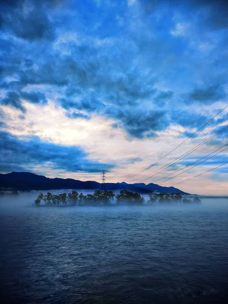 Tiro Vertical Céu Azul Nublado Sobre Mar Árvores Cobertas Nevoeiro — Fotografia de Stock