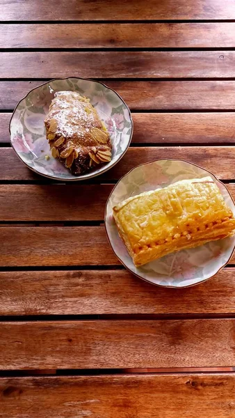 扁平的杏仁羊角面包和膨松的金枪鱼糕点垂直铺在一张木制桌子上 — 图库照片
