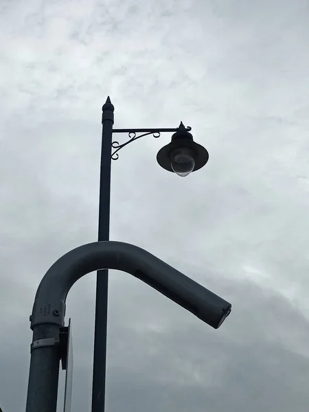 A vertical shot of a street lamp on the road in daylight in cloudy sky background