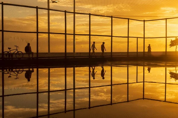 stock image Silhouette of people exercising on the edge of Rio Vermelho beach in Salvador, Bahia, against yellow sunset.