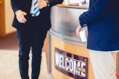 Takım elbiseli iki kişi bir etkinliğin girişindeki karşılama merkezinde iletişim kuruyor.