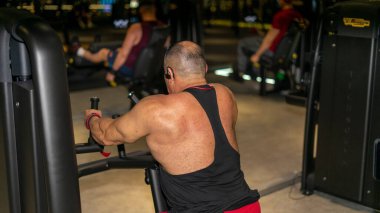 Spor salonunda beyaz kaslı bir adam antrenman yapıyor..