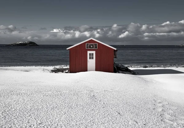 ノルウェー北部の曇り空の下で穏やかな海を満たす雪原の小さな赤いキャビン — ストック写真