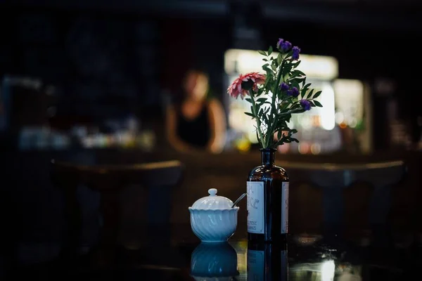 背景にぼんやりした人と砂糖のポットの横にあるカフェテーブルの上に花の花瓶やヒップスターバーで機嫌の良い照明 — ストック写真