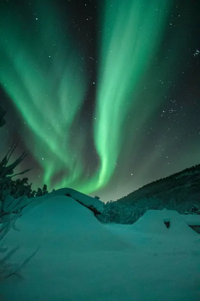 雪に覆われたノルウェーの丘の上の暗い星空の間で 極性の光の垂直長時間露光 — ストック写真
