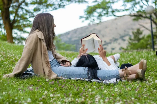 Zbliżenie Kobiety Leżącej Nogach Przyjaciółki Czytającej Książkę Trawie — Zdjęcie stockowe