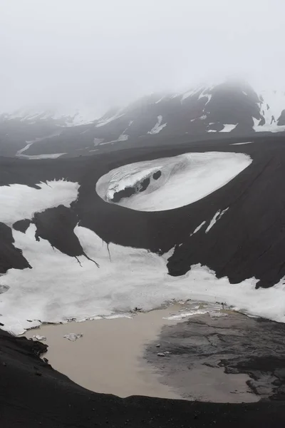 南極の霧の中で雪のピークを失った背の高い岩の山の下の凍結池 — ストック写真