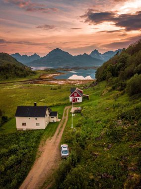 Norveç 'in kuzeyinde deniz ve dağların olduğu yeşil bir arazide küçük evler ve arabaların dikey görüntüsü.