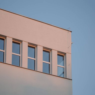 Mavi gökyüzü arka planına bakan pencereli bir bina köşesi.