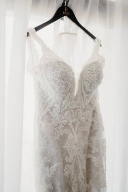 Pencerede asılı bir askıda asılı güzel dantelli bir gelinliğin dikey çekimi.