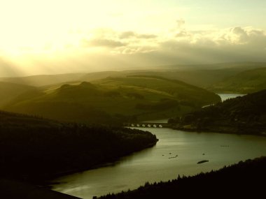 Akşamları güneşin altında tepelerle çevrili bir göl manzarası.