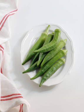 Beyaz masada bir tabak çiğ bamyanın dikey görüntüsü.