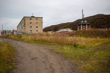 Çimenli asfaltsız yol ve Murmansk, Rusya 'da bulutlu gökyüzünün altında yeşil dağlara yakın bir bina.