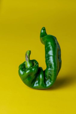 Sarı arka planda izole edilmiş yeşil biberin dikey görüntüsü.