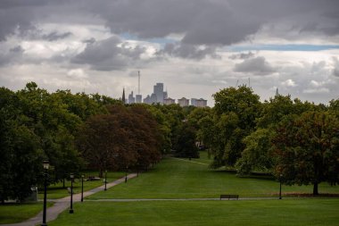 Yeşil çimenler ve yüksek binaların arka planına sahip ağaçlarla çevrili güzel bir park manzarası.
