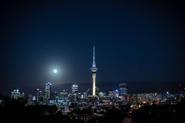 Auckland 'ın ufuk çizgisi. Işıklı binalar ve gece gökyüzünde dolunay.