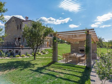 Bahçedeki ahşap bir pergola yanında geniş bir ahşap ve taş bina görüntüsü..
