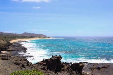 Mavi gökyüzü altında kayalık kıyı şeridi ve köpüklü dalgaların manzarası
