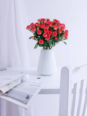 Üzerinde dergi olan beyaz bir vazoda güzel bir gül buketinin dikey görüntüsü.