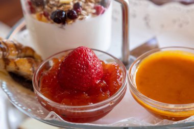 Çilek reçelinin yatay yakın çekimi ve bir diğeri de beyaz tabakta bir kurabiyeyle turuncu.