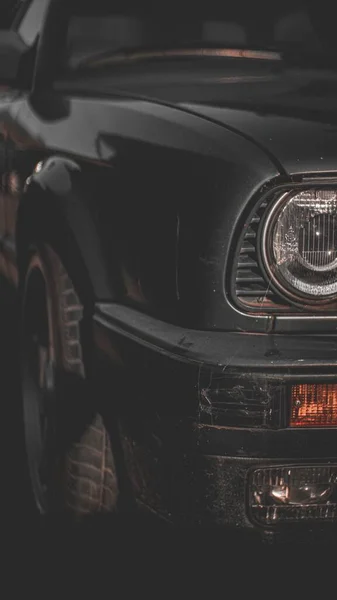 Pionowe Zbliżenie Reflektorów Czarnego Samochodu Zaparkowanego Pod Słońcem — Zdjęcie stockowe