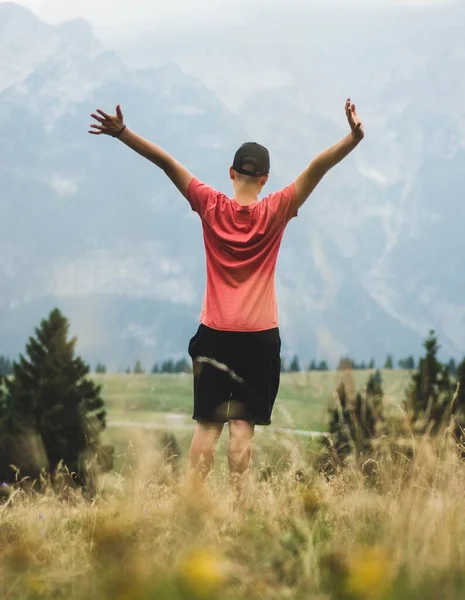 一个年轻的男性高举双手欣赏高山美景的垂直镜头 — 图库照片