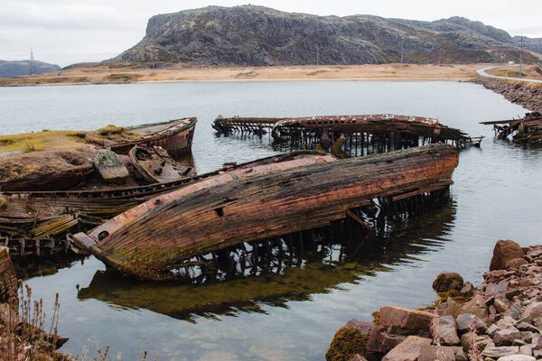 Деревянный пирс у реки Кола с холмами под серым облачным небом в Мурманске, Россия